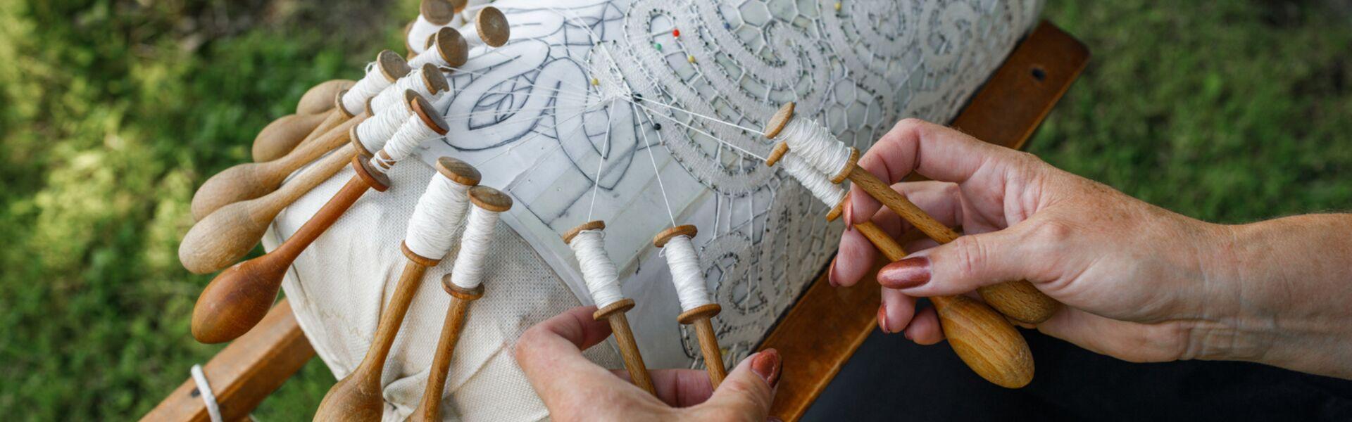 A lace roller with a pattern, thread bobbins and the beginnings of a lace pattern.