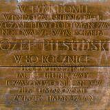 Tekst wyryty na drewnie - W dniach 7/8 grudnia 1914 roku w czasie bitwy pod Limanową nocował ze swym sztabem Józef Piłsudski. W 80. rocznicę tego wydarzenia tablice ufundowały Towarzystwo Miłośników Ziemi Limanowskiej Związek Limanowian