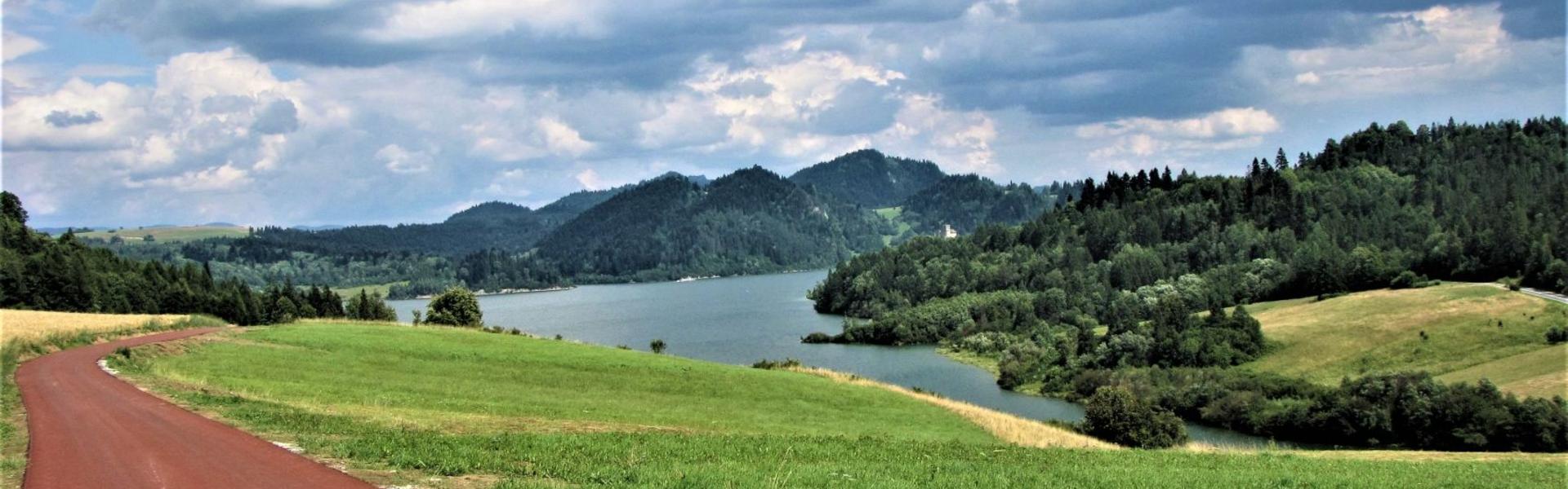 Widok na zalesione Pieniny i jezioro Czorsztyńskie, po lewej wzdłuż jeziora biegnie ścieżka rowerowa.